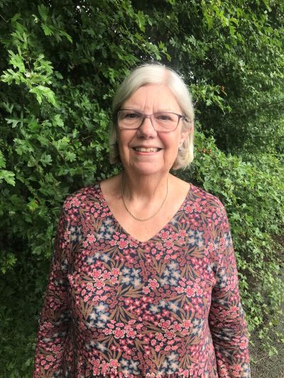 Bridget Thurgood from the waist up in a floral top standing in front of a hedge.